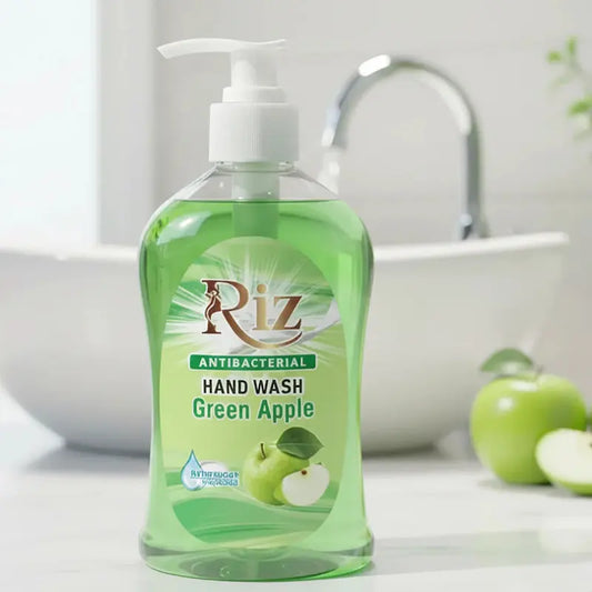 Clear bottle of Riz Antibacterial Hand Wash with green liquid and a white pump, featuring a green apple scent, sitting on a white bathroom counter near a sink and fresh green apples.