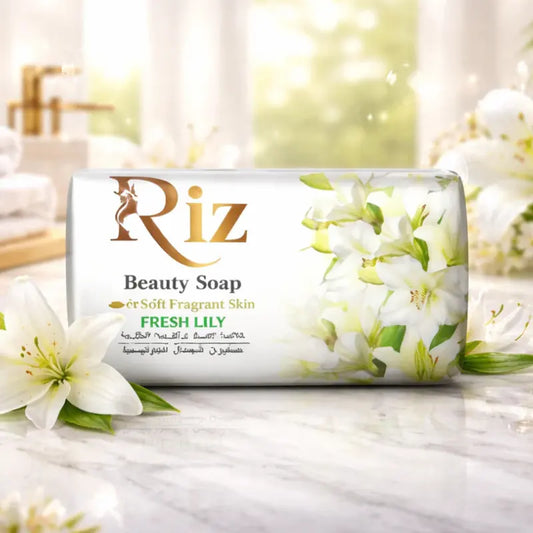 A bar of Riz Beauty Soap featuring a Fresh Lily scent, packaged in a white wrapper decorated with elegant white lilies. The soap is displayed on a luxurious marble surface with real lilies and a soft focus bathroom background.